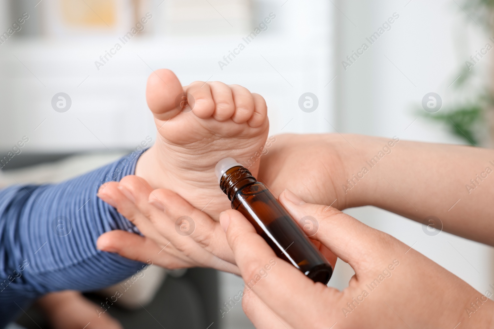 Photo of Mother applying essential oil from roller bottle onto her baby`s heel indoors, closeup