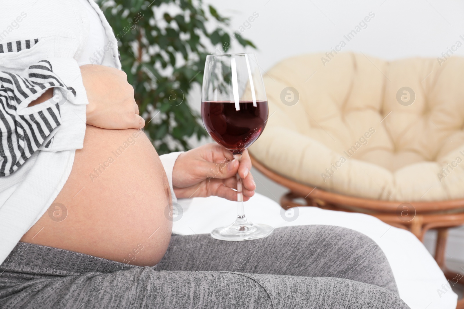 Photo of Pregnant woman with glass of red wine at home. Alcohol addiction