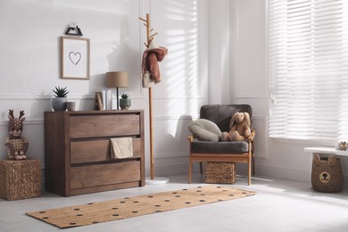 Stylish room interior with wooden chest of drawers and comfortable armchair