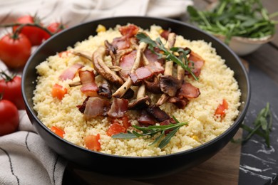 Photo of Tasty couscous with mushrooms and bacon in bowl on table, closeup