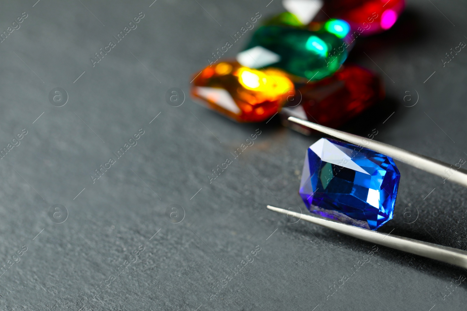 Photo of Tweezers with beautiful gemstone on grey table. Space for text