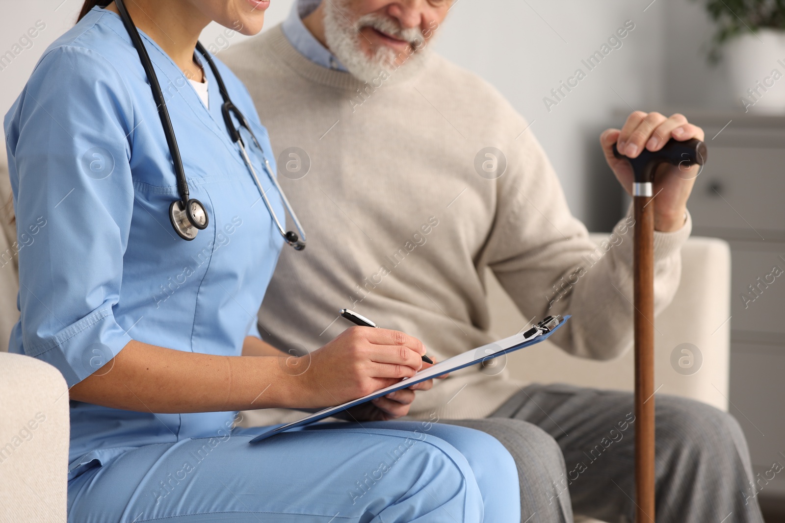 Photo of Nurse with clipboard assisting elderly patient in hospital, closeup