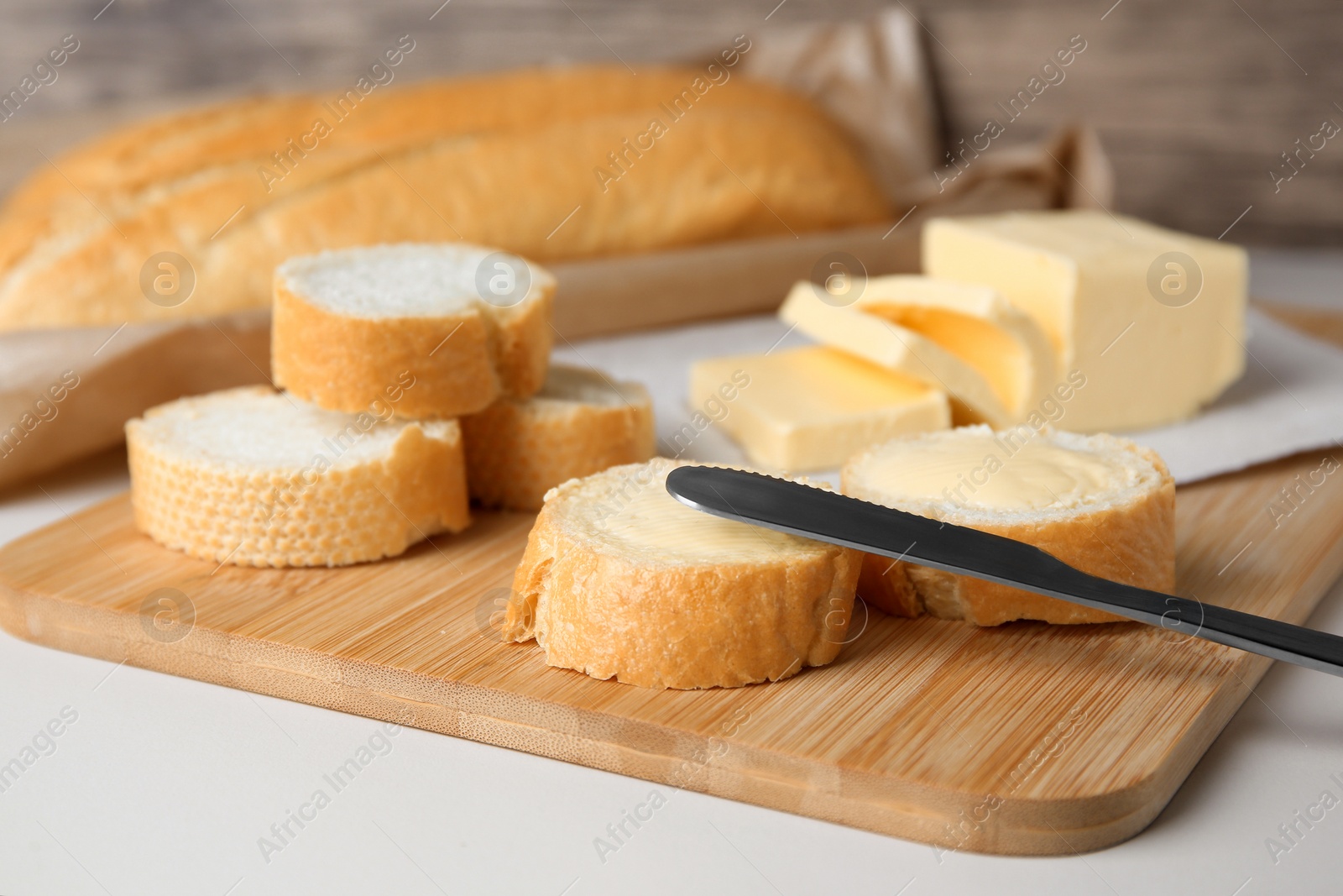 Photo of Tasty cut baguette with fresh butter on white table, closeup