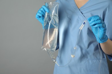 Nurse with IV infusion set on grey background, closeup