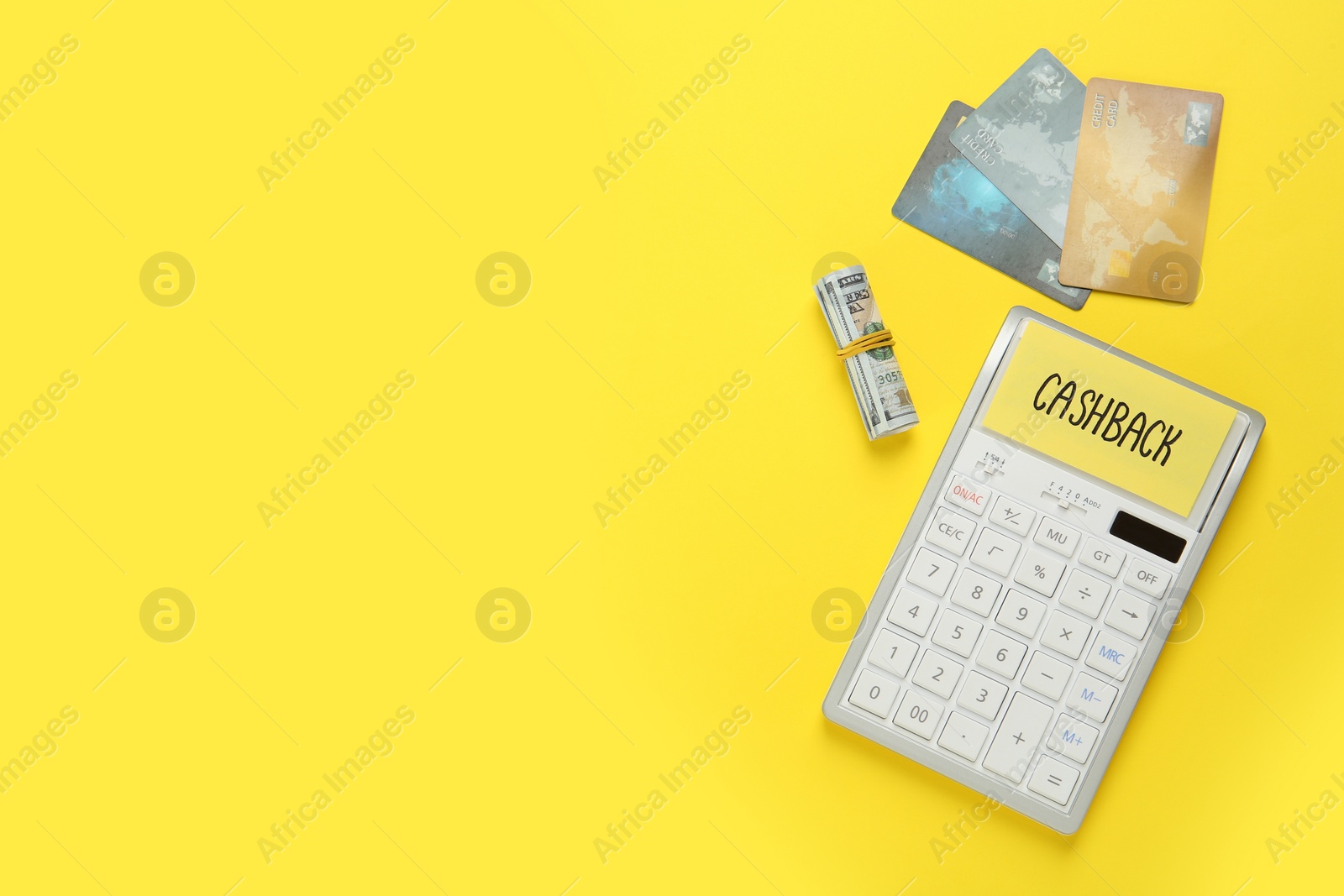 Photo of Calculator, credit card and rolled dollar banknotes on yellow background, flat lay with space for text. Cashback concept