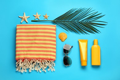 Beach towel, sunglasses and sun protection products on light blue background, flat lay