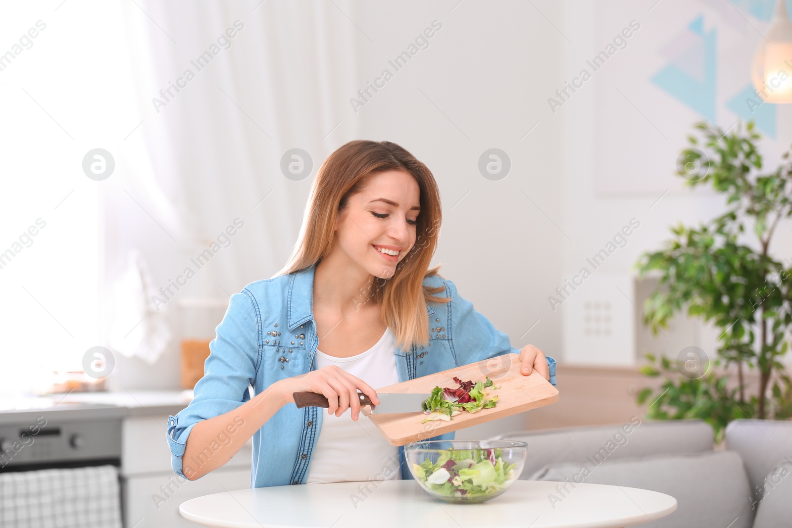 Photo of Happy young woman preparing salad in kitchen. Healthy diet