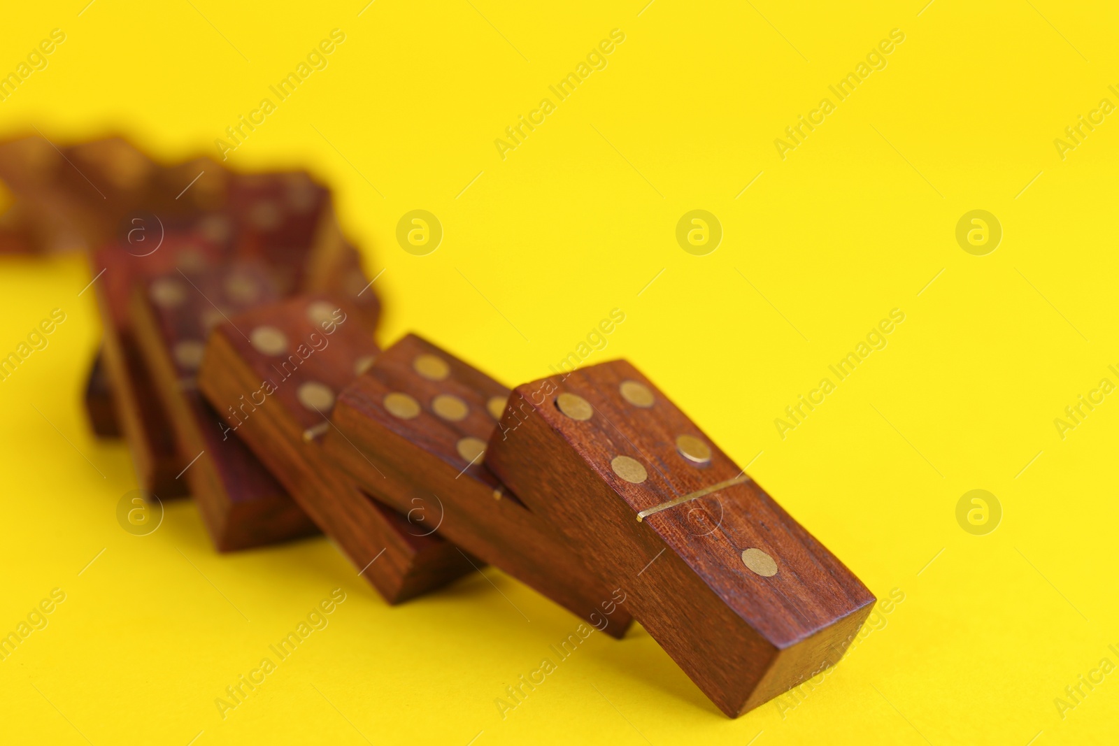 Photo of Falling wooden domino tiles on yellow background, closeup