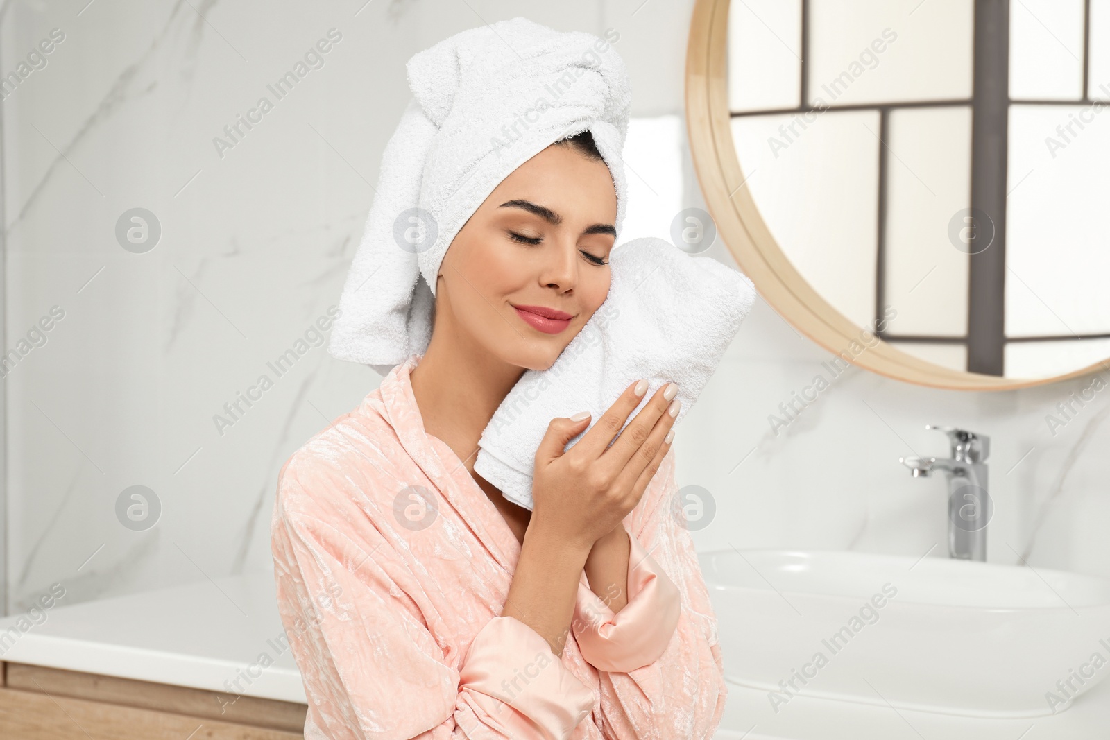 Photo of Young woman wiping face with towel in bathroom