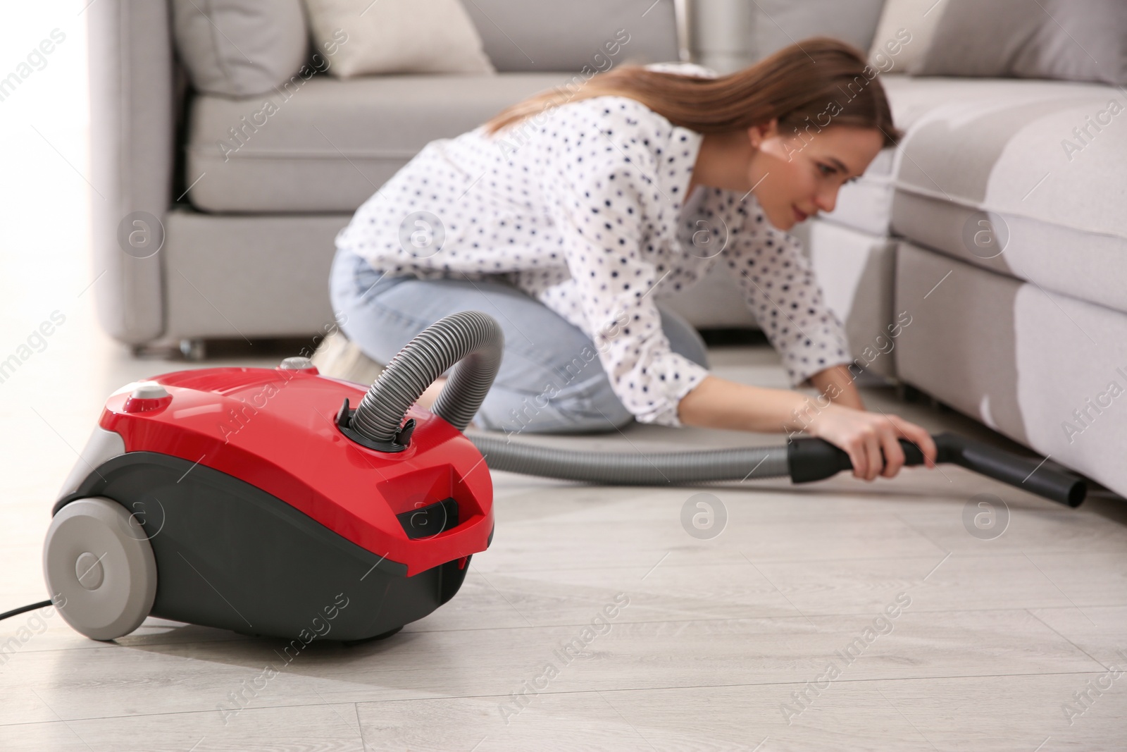 Photo of Young woman using vacuum cleaner at home