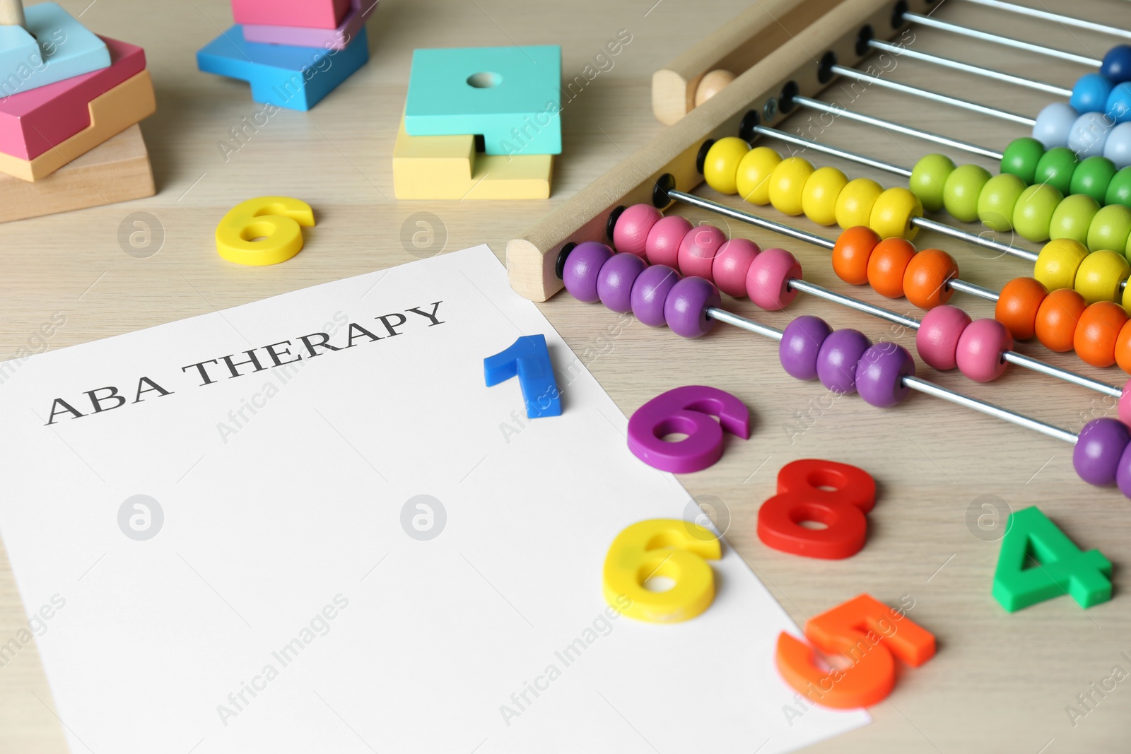 Photo of Paper sheet with abbreviation ABA (Applied behavior analysis), abacus and colorful numbers on white wooden table