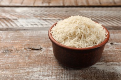 Photo of Raw basmati rice in bowl on wooden table, space for text