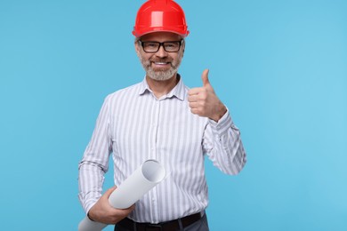 Photo of Architect in hard hat holding draft and showing thumb up on light blue background