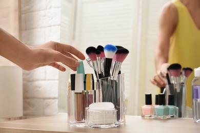 Woman taking mascara from organizer for makeup cosmetic products on table