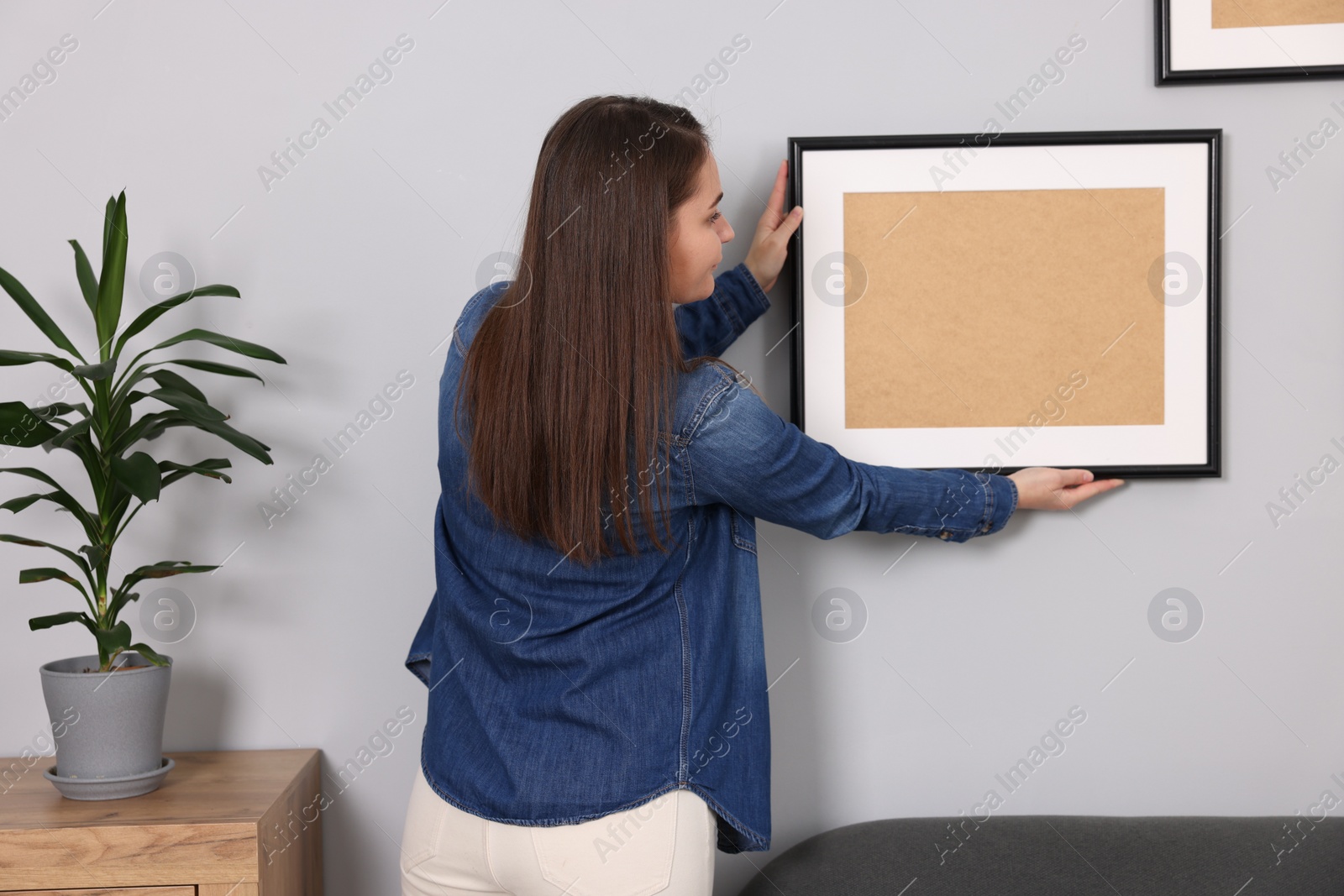 Photo of Woman hanging picture frame on gray wall at home