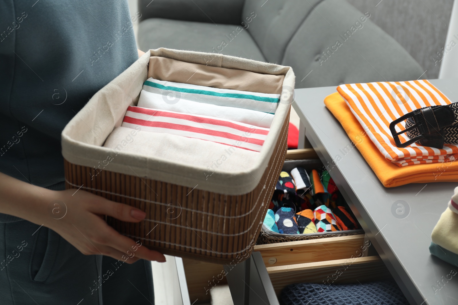 Photo of Woman holding basket with folded clothes indoors, closeup