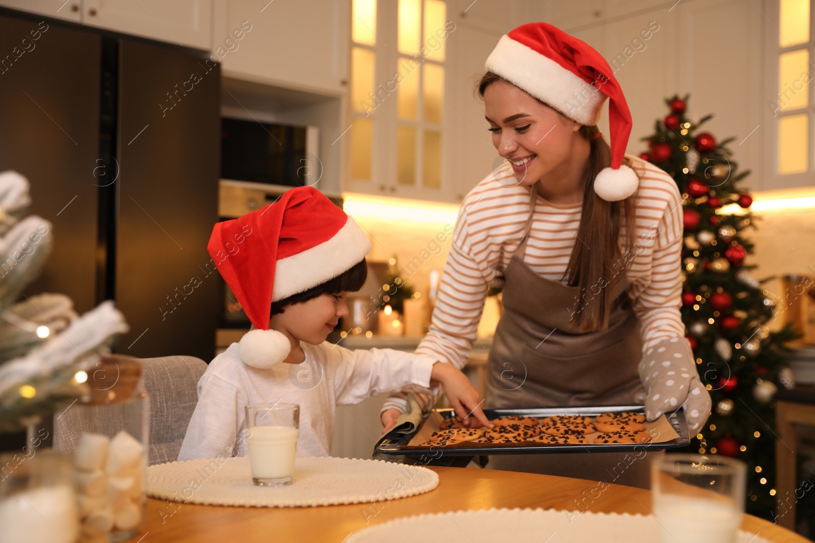 Photo of Mother giving her cute little son freshly baked Christmas cookie in kitchen