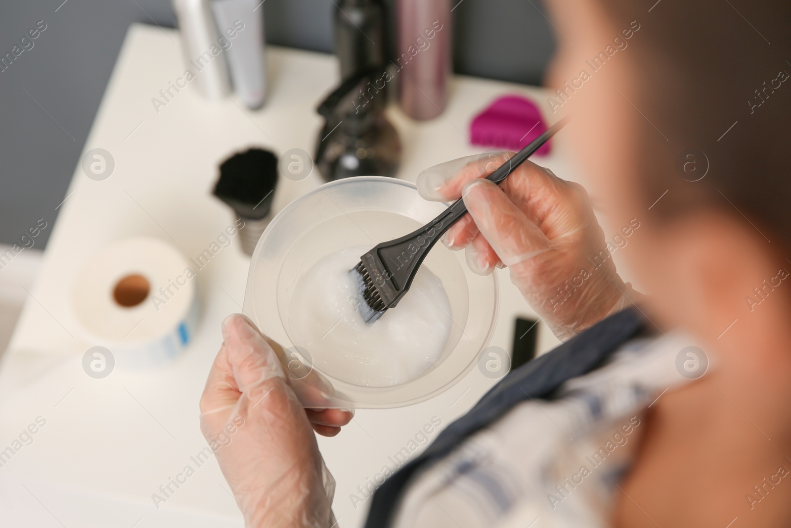 Photo of Professional hairdresser holding bowl with hair dye in beauty salon, closeup