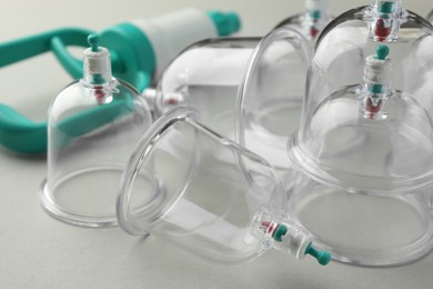 Photo of Plastic cups and hand pump on light grey background, closeup. Cupping therapy