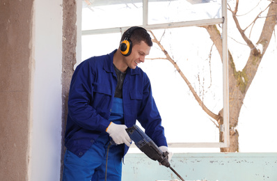 Photo of Worker using rotary drill hammer for window installation indoors