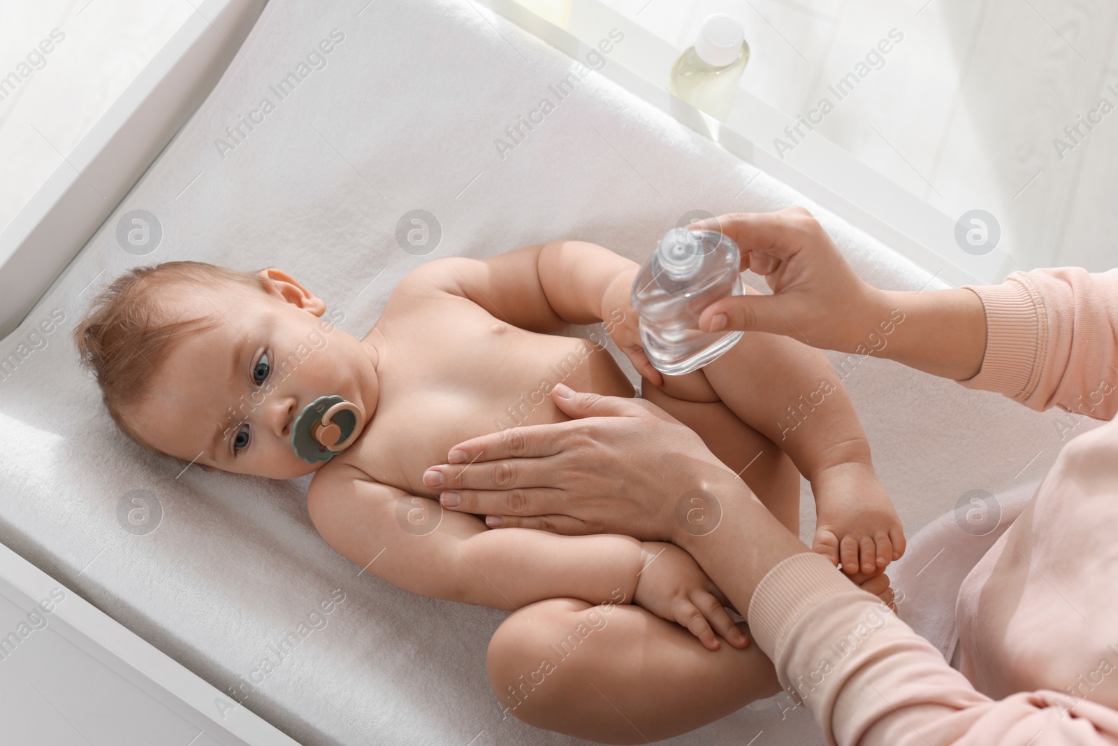 Photo of Mother massaging her cute baby with oil on changing table, above view