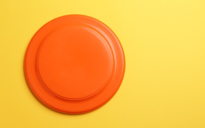 Photo of Orange plastic frisbee disk on yellow background, top view. Space for text
