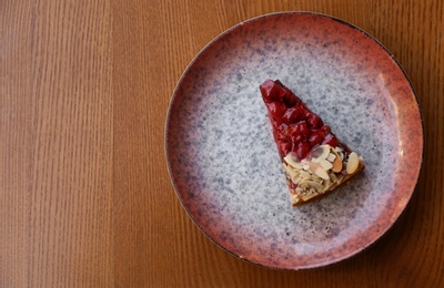 Photo of Plate with slice of cherry cake on wooden table, top view