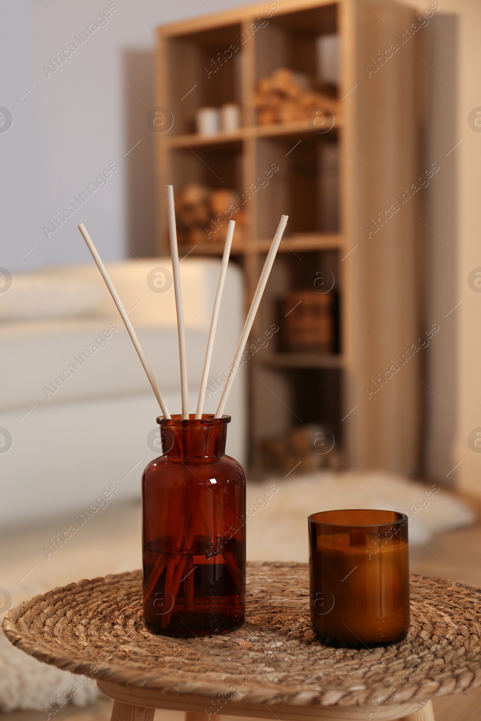 Photo of Aromatic reed air freshener and candle on wicker tray in room