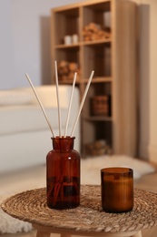 Photo of Aromatic reed air freshener and candle on wicker tray in room