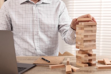 Photo of Playing Jenga. Man building tower with blocks at wooden table in office, closeup