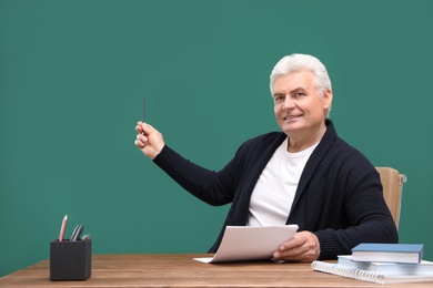 Photo of Portrait of senior teacher pointing on green chalkboard at table