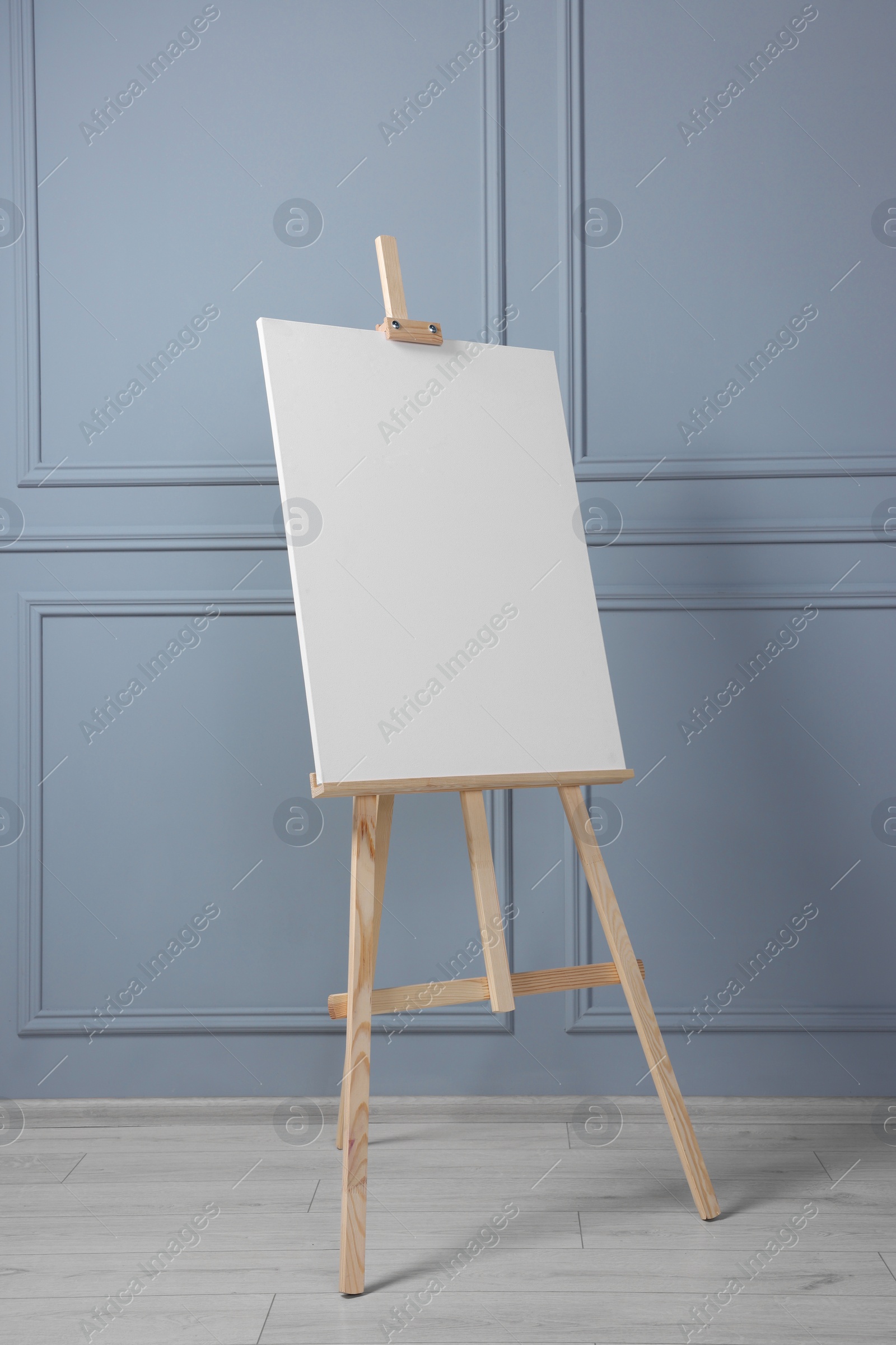 Photo of Wooden easel with blank canvas near grey wall indoors. Space for text