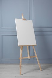 Photo of Wooden easel with blank canvas near grey wall indoors. Space for text