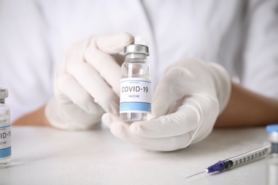 Doctor holding vial with vaccine against Covid-19 at table, closeup