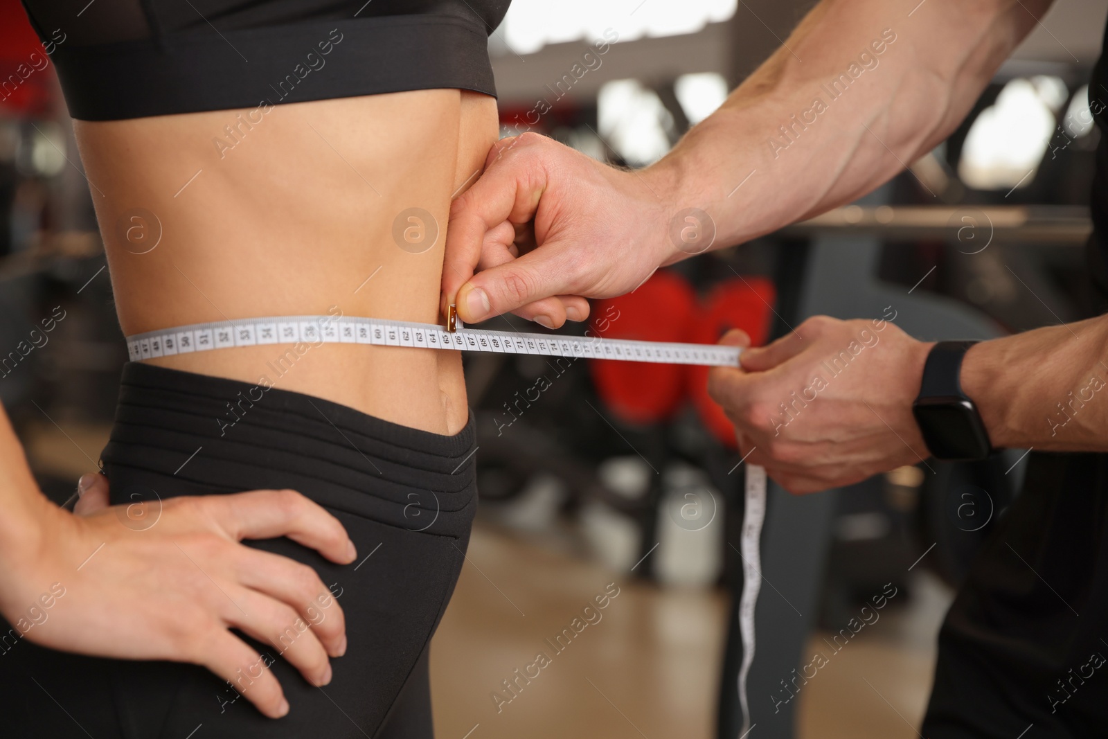 Photo of Trainer measuring woman`s waist with tape in gym, closeup