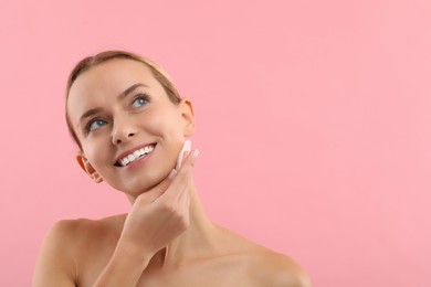 Photo of Smiling woman removing makeup with cotton pad on pink background. Space for text