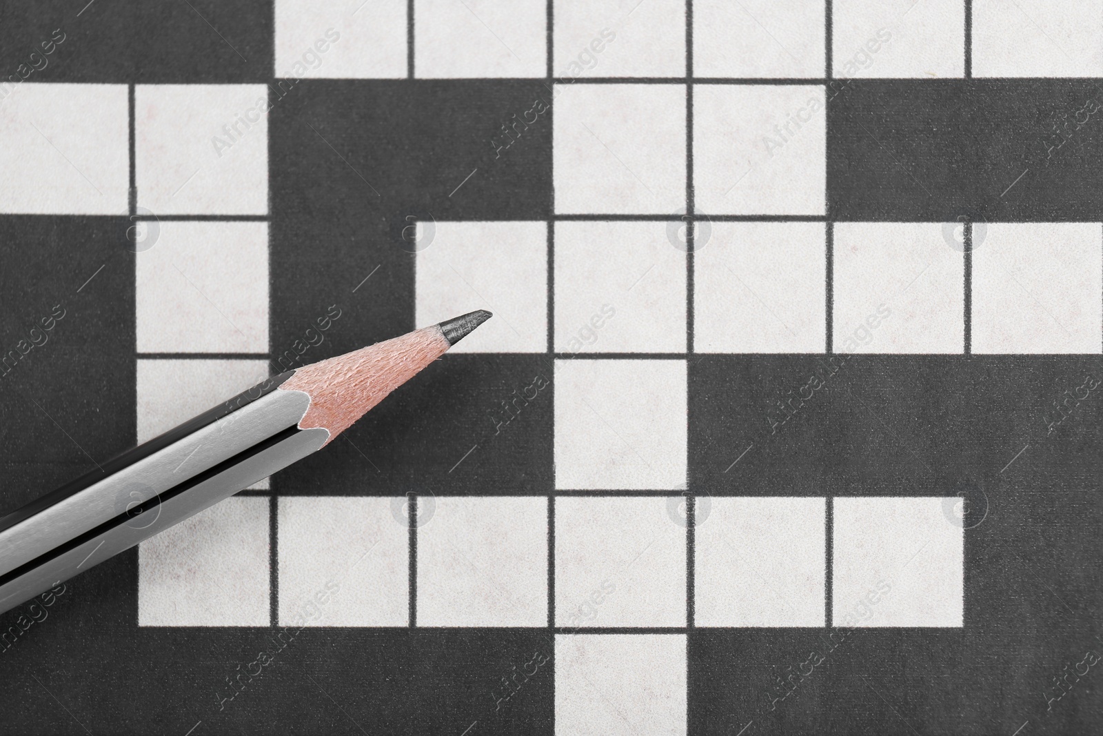 Photo of Pencil on blank crossword, top view. Space for text