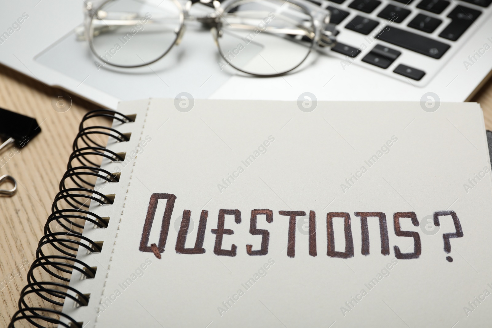 Photo of Word QUESTIONS written in notebook on wooden table, closeup