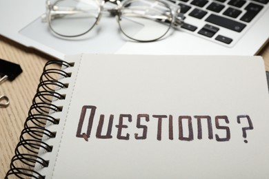 Photo of Word QUESTIONS written in notebook on wooden table, closeup