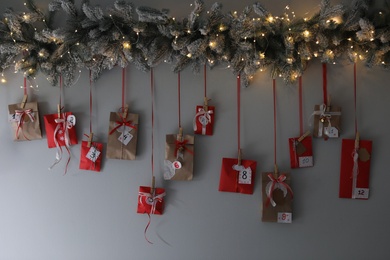 Photo of Christmas advent calendar with decorative fir branches and fairy lights hanging on wall