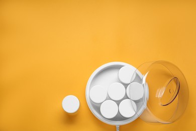 Modern yogurt maker with jars on orange background, flat lay. Space for text