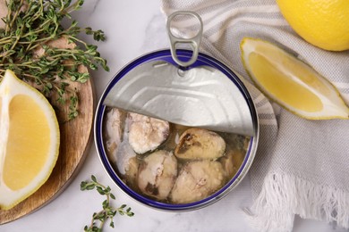 Photo of Open tin can with mackerel chunks, lemon and thyme on white marble table, flat lay