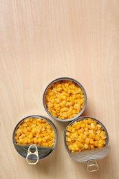 Open tin cans of sweet corn on wooden table, flat lay with space for text