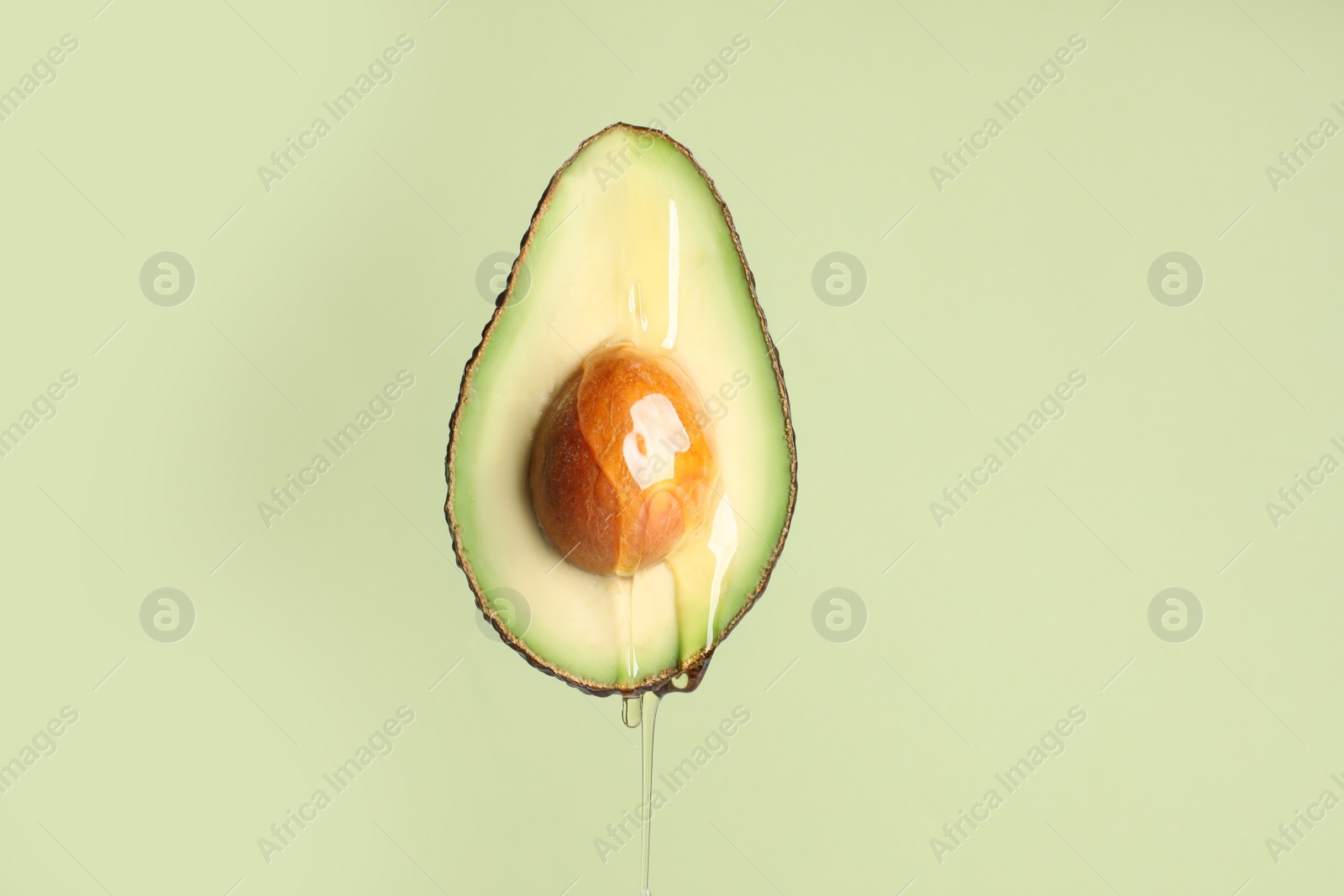 Photo of Pouring essential oil onto cut avocado on light green background