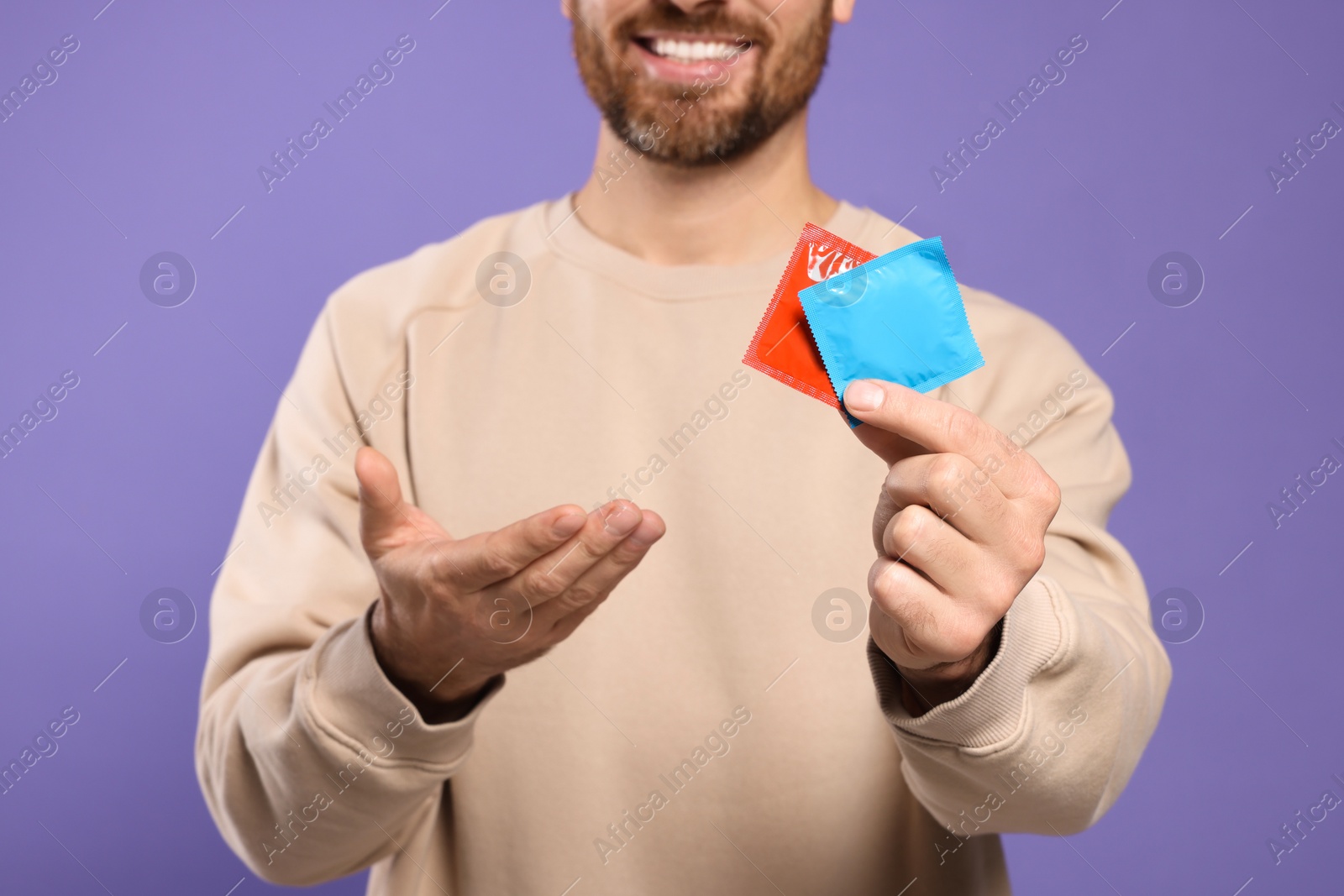 Photo of Man holding condoms on purple background, closeup. Safe sex