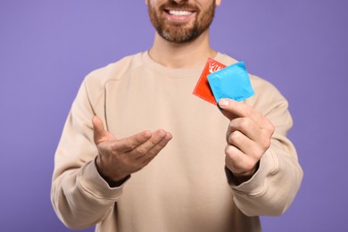 Photo of Man holding condoms on purple background, closeup. Safe sex