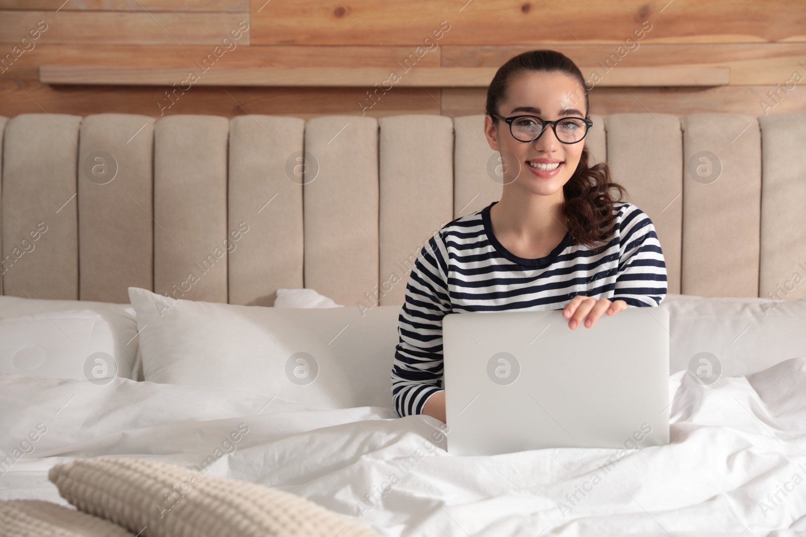 Photo of Young woman working with laptop on bed at home