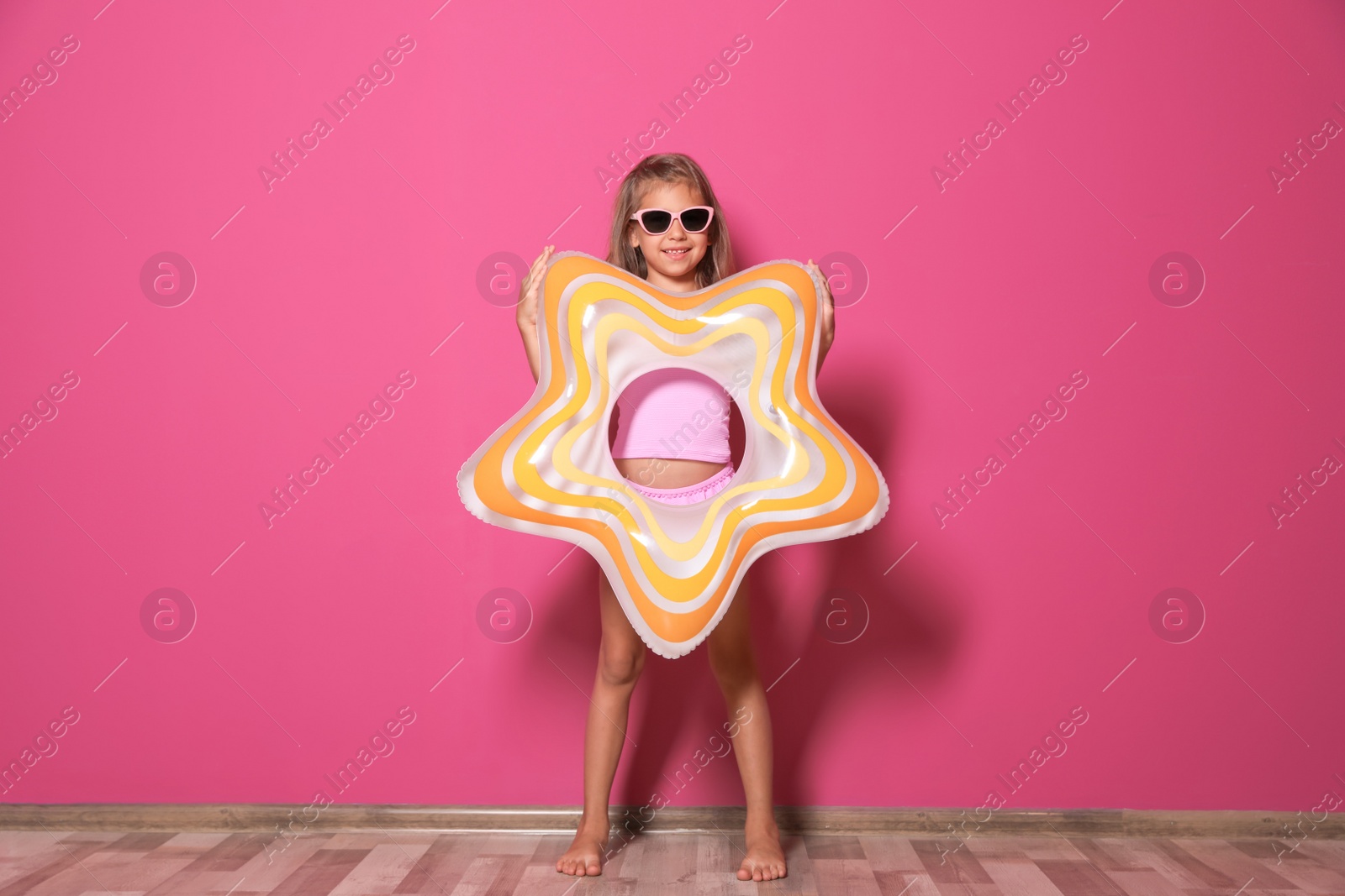 Photo of Cute little girl with bright star shaped inflatable ring near color wall