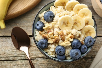 Photo of Tasty oatmeal with banana, blueberries and walnuts served in bowl on wooden table, flat lay