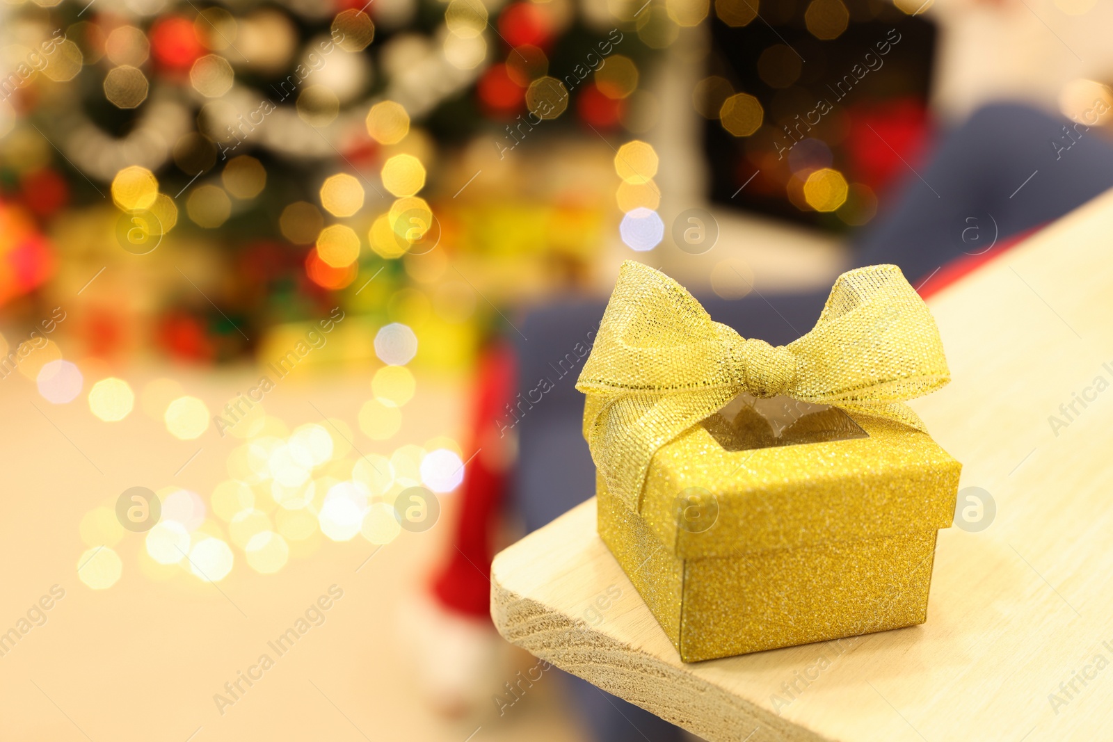 Photo of Golden gift box on wooden shelf against blurred festive lights, space for text. Christmas celebration